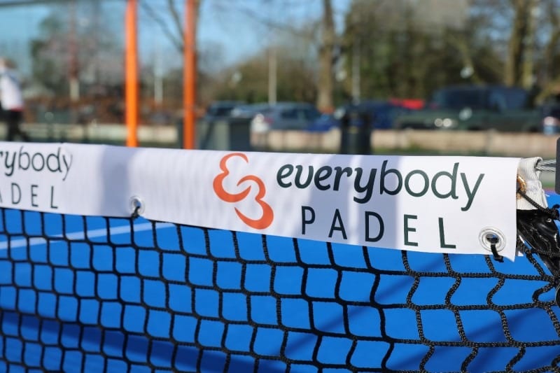The Everybody Padel banner on the net of a built court, with the car park out of focus behind