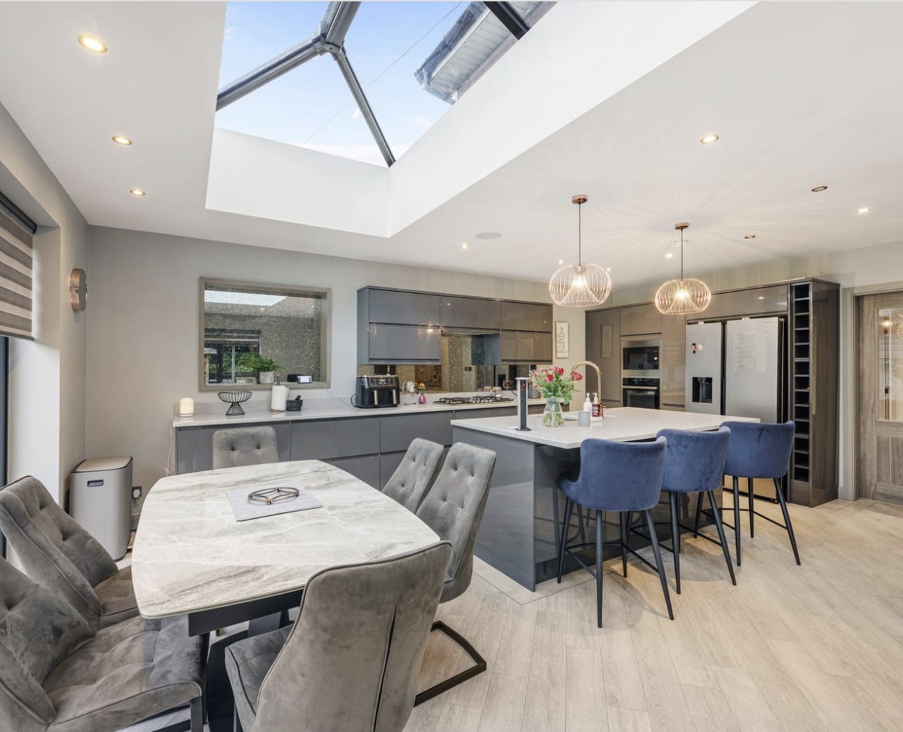 The kitchen and family room of the house, lit by a roof lantern, with an island and a dining table on a pale timber-effect floor